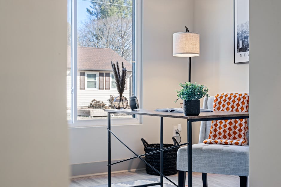 Bright modern home office with a minimalist desk, lamp, and cozy blanket by the window.